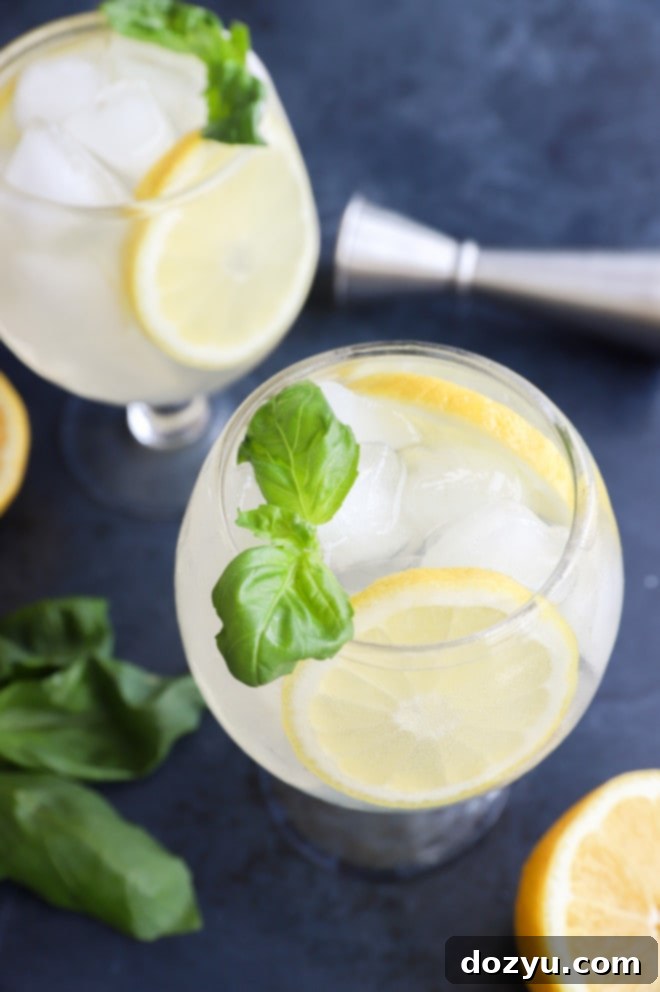 A elegant goblet filled with a lemon basil cooler cocktail, garnished with a vibrant basil sprig and lemon slice.