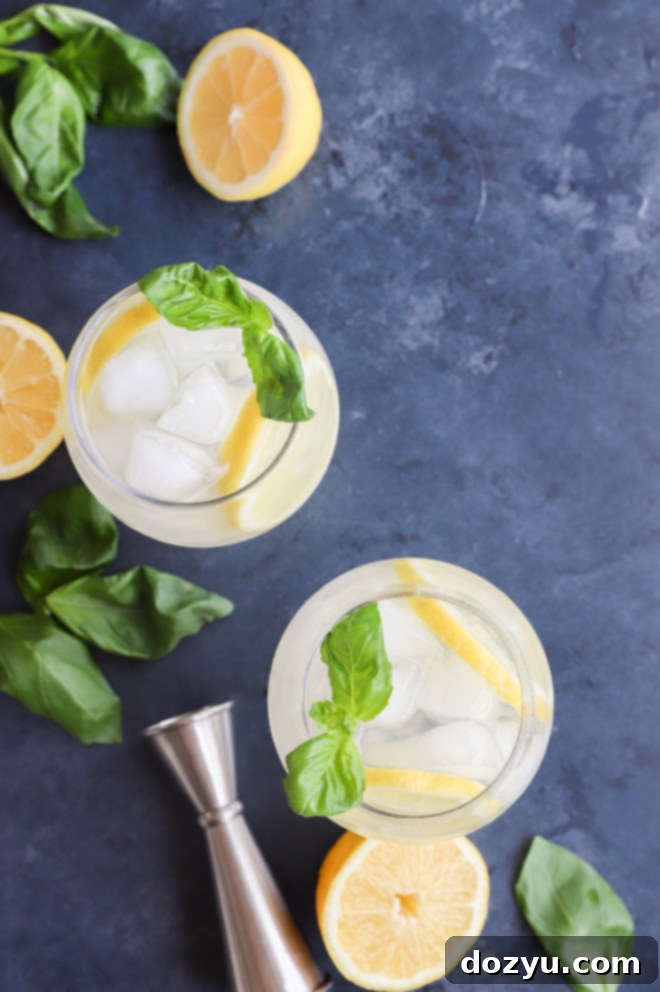 Overhead shot of several lemon basil cooler cocktails, garnished with lemon and basil, arranged on a rustic table.