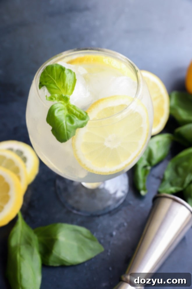 Close-up of a Lemon Basil Cooler cocktail in a glass, garnished with a basil sprig and lemon wheel, showcasing its freshness.