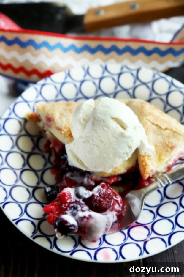 A fork taking a generous bite from a slice of triple berry galette, showcasing the juicy berry filling and golden crust.