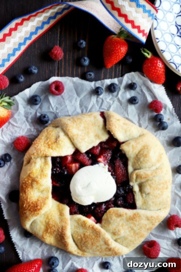 A beautiful triple berry galette, fresh out of the oven, with a perfectly golden-brown, pleated crust and bubbling berry filling.