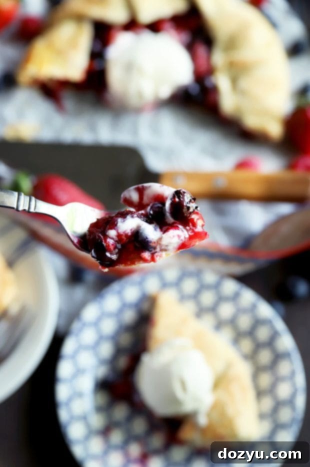 A close-up shot of a fork digging into a slice of triple berry galette, showing the juicy fruit filling and tender crust.