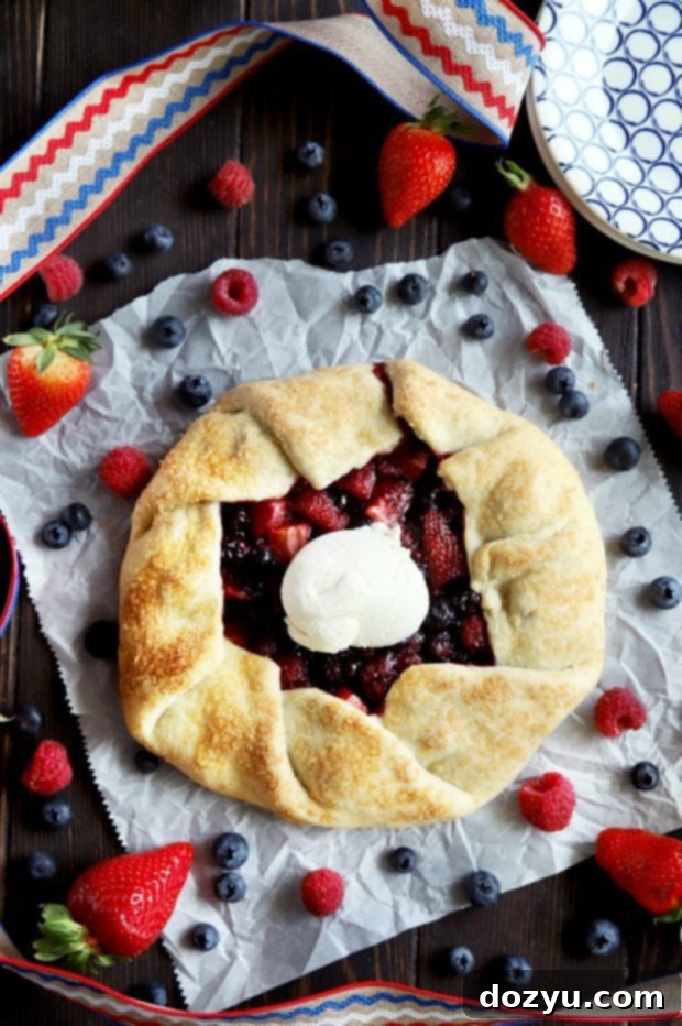 An unbaked Raspberry, Blueberry, and Strawberry Galette resting on parchment paper on a baking sheet, ready for the oven.
