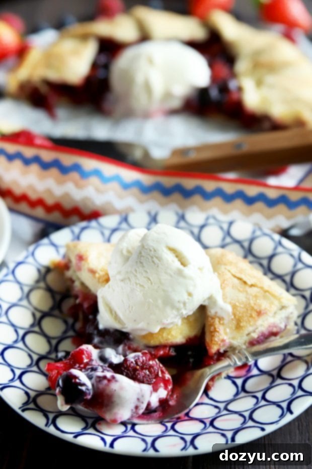 A close-up of a slice of triple berry galette with a fork taking a bite, emphasizing the juicy berries and flaky crust.
