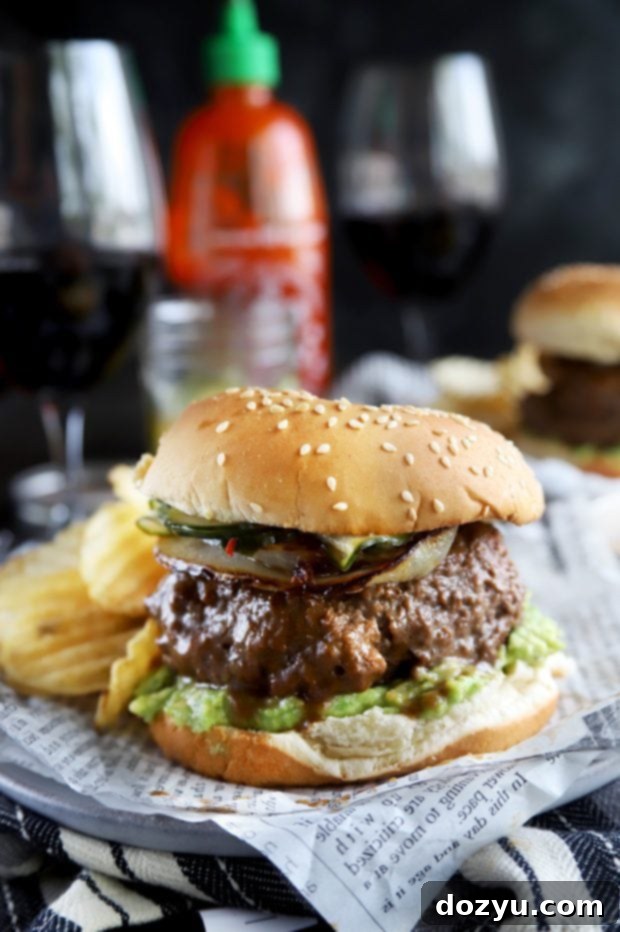 A close-up of a gourmet Sriracha burger, showcasing the glossy miso glaze, fresh toppings, and toasted bun.