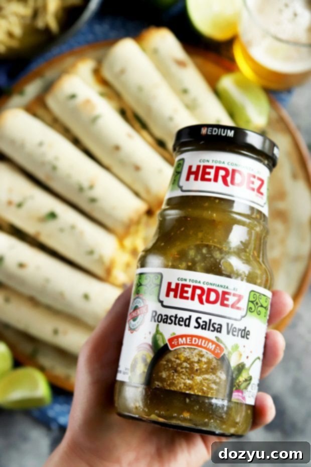 A hand holding a jar of HERDEZ salsa verde, emphasizing the key ingredient for this taquito recipe