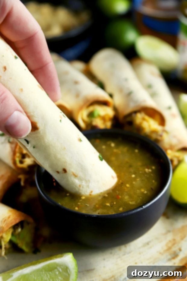 Hand dipping a golden-brown taquito into a small bowl of fresh salsa verde