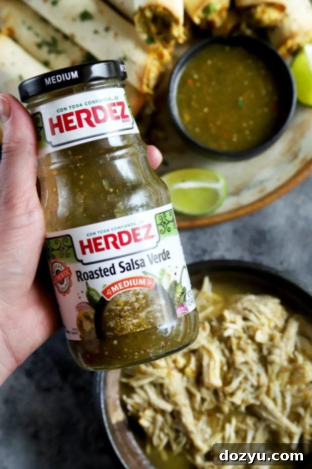 Holding a jar of HERDEZ Roasted Salsa Verde above shredded chicken for taquito preparation