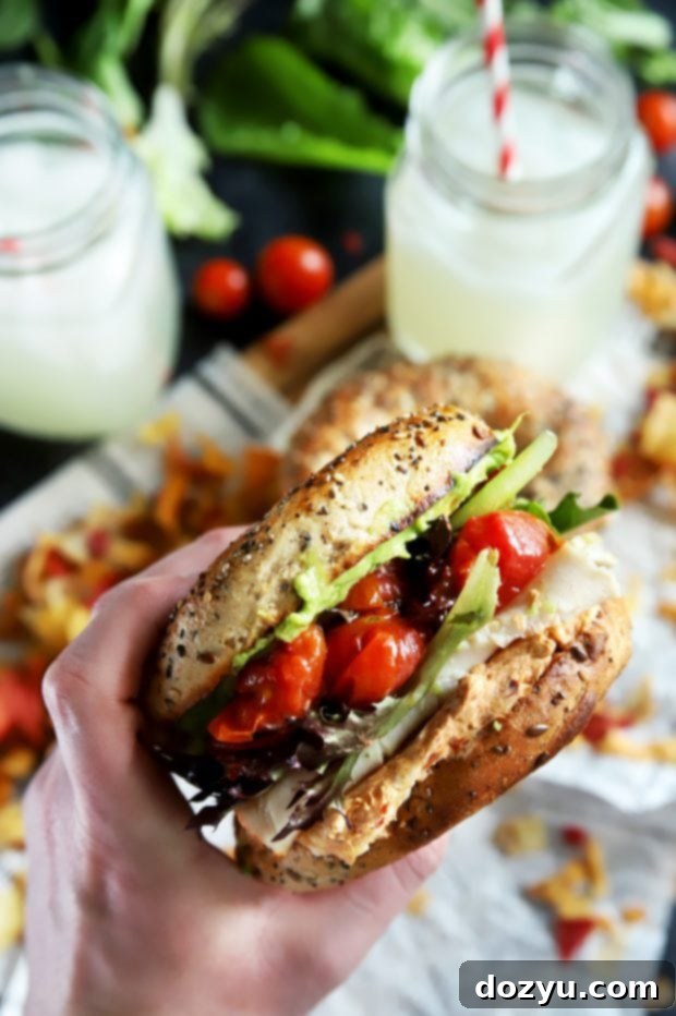 Hand holding a bagel sandwich with turkey and vegetables
