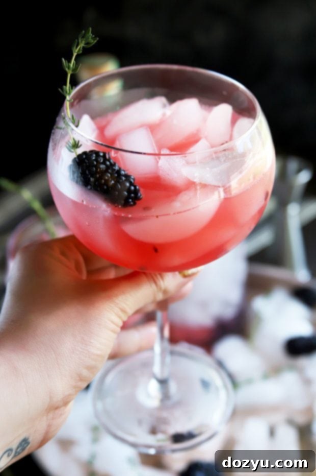 Holding a gin cocktail with blackberry and thyme garnish