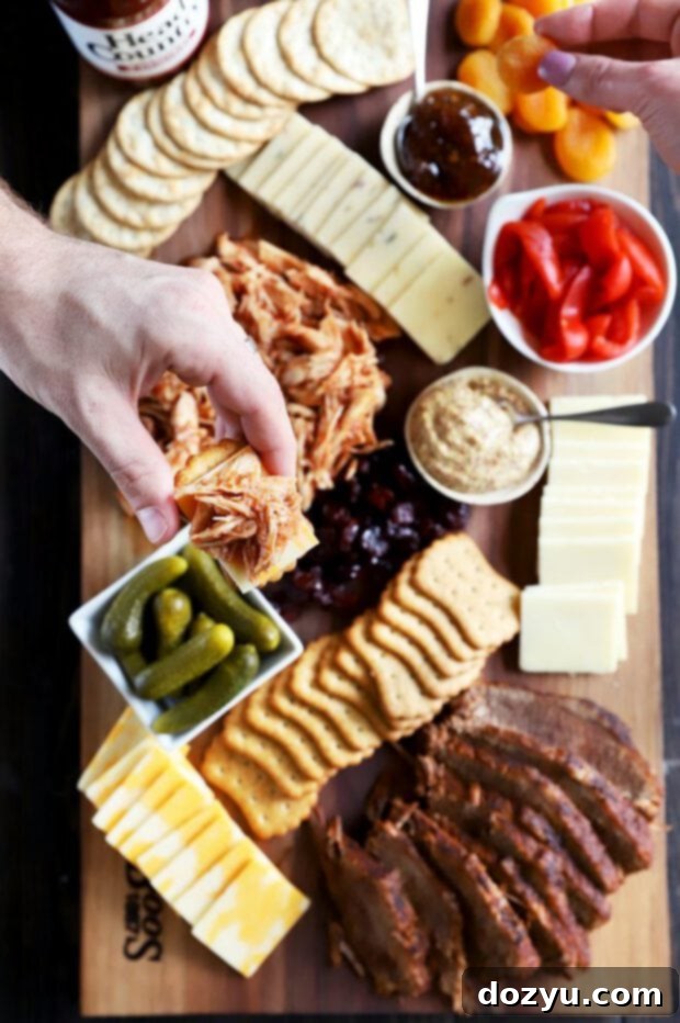 A hand holding a cracker topped with BBQ meat and a slice of cheese.
