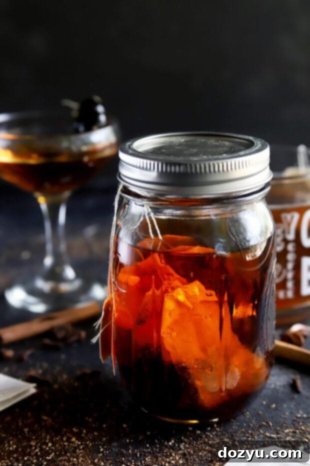 A styled photo featuring a glass of cocktail, a bottle of bourbon, and a mug with chai tea bags, all against a cozy, autumn-themed backdrop.