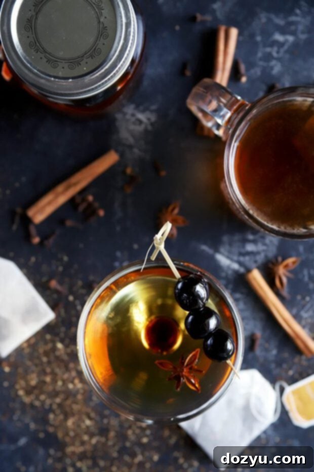 Overhead view of a Manhattan cocktail, garnished with a cherry, made with chai-infused bourbon, on a rustic wooden surface, highlighting the rich color and inviting presentation.