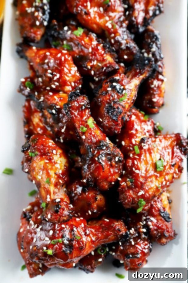 Crispy grilled Korean BBQ wings on a white platter with sesame seeds and green onion