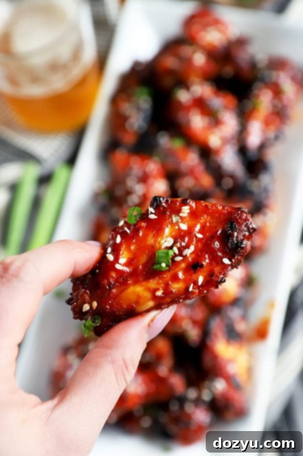 Hand holding a wing with Korean BBQ sauce on it, sesame seeds, and green onion
