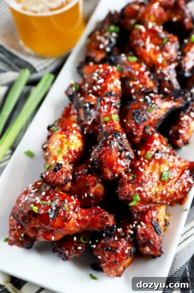 Wings slathered in Korean BBQ sauce on a white platter with beer in the background