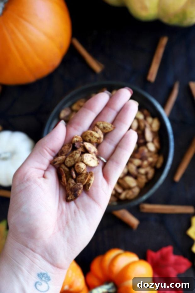 A hand reaching into a bowl, scooping out a generous handful of golden-brown, perfectly seasoned roasted pumpkin seeds.