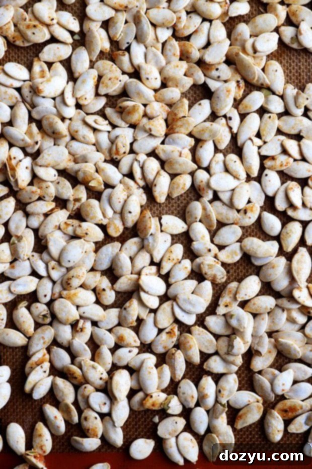 Overhead view of cleaned, seasoned pumpkin seeds spread out evenly on a parchment-lined baking sheet, ready for roasting.