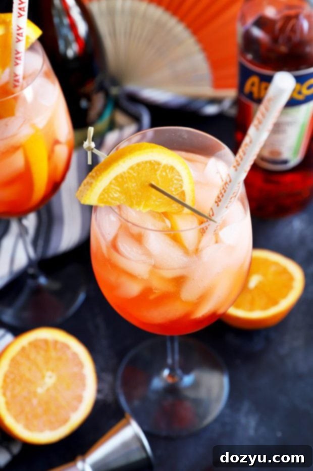 A vibrant orange Aperol Spritz cocktail, served in a large wine glass with ice and an orange slice garnish, ready to be enjoyed.
