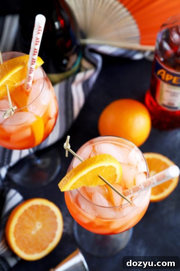 Two vibrant orange Aperol spritz cocktails with ice and orange slices, served in classic stemmed wine glasses against a rustic background, suggesting a relaxed social setting.