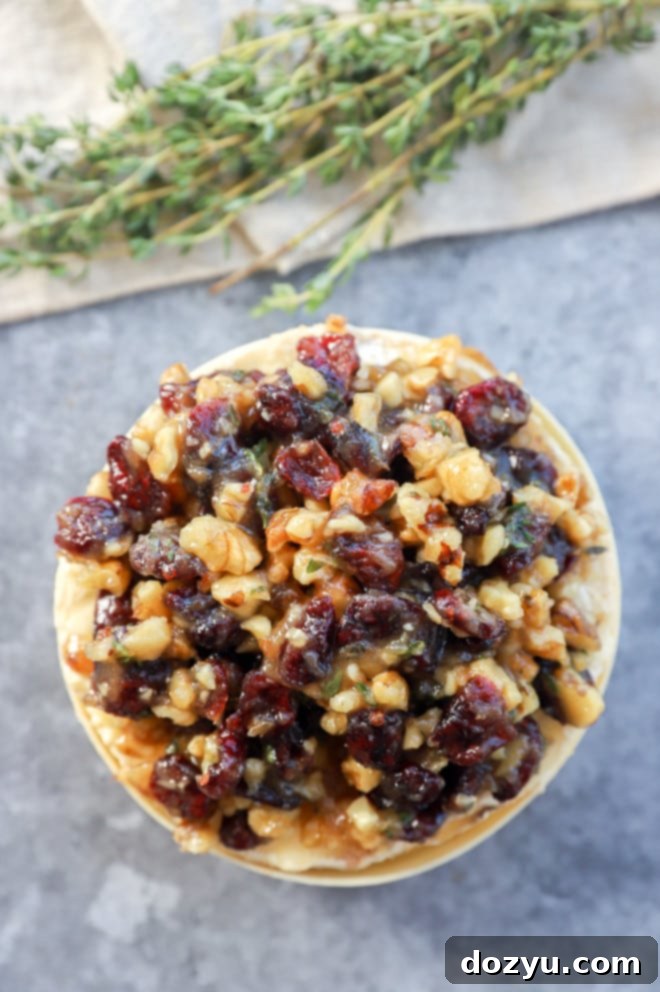 Baked camembert in wooden box before baking, with cranberry and walnut topping