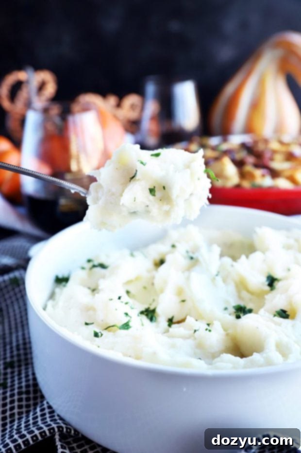 A serving spoon lifting creamy Instant Pot Mashed Potatoes from a bowl.