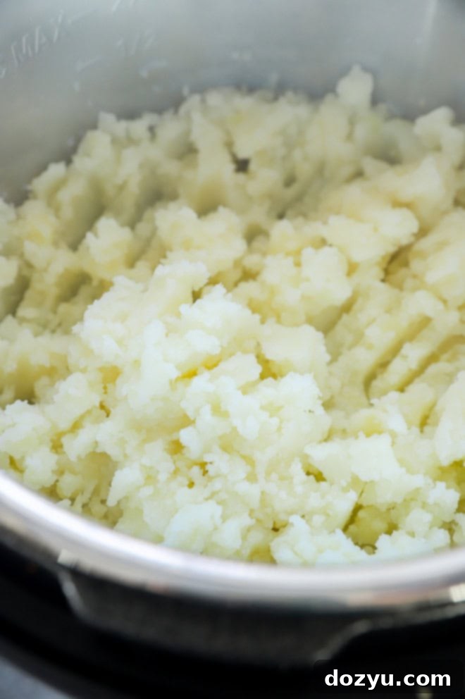 Mashed potatoes being stirred in the Instant Pot insert after cooking.