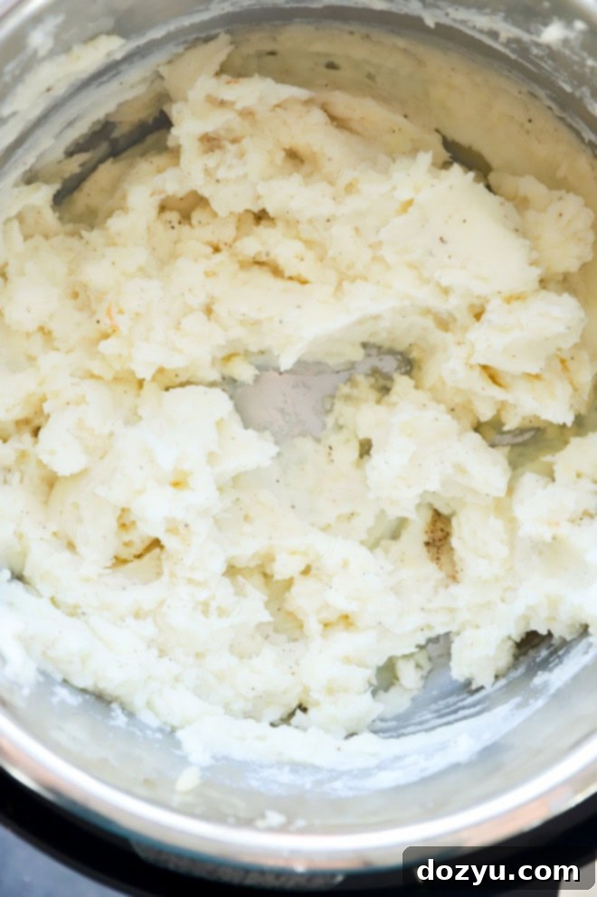 Instant Pot Mashed Potatoes mixed with butter, cheese, and roasted garlic in the Instant Pot insert.