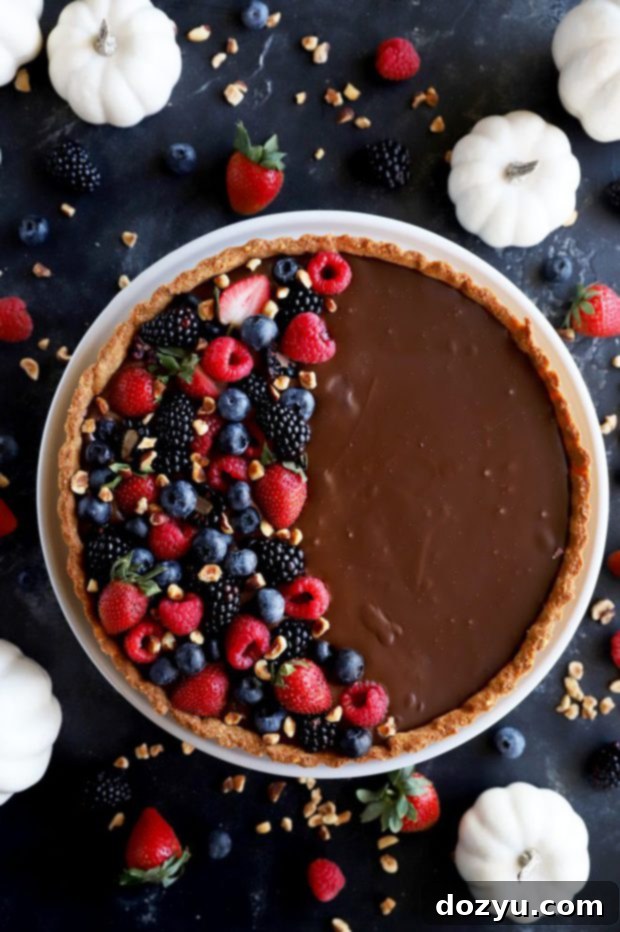 Overhead photo of a ganache tart, elegantly decorated with fresh berries and chopped hazelnuts.