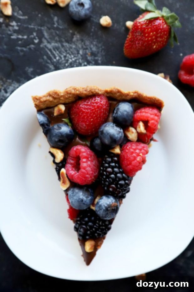 A perfectly portioned slice of chocolate tart, revealing the creamy ganache and hazelnut crust, topped with berries.