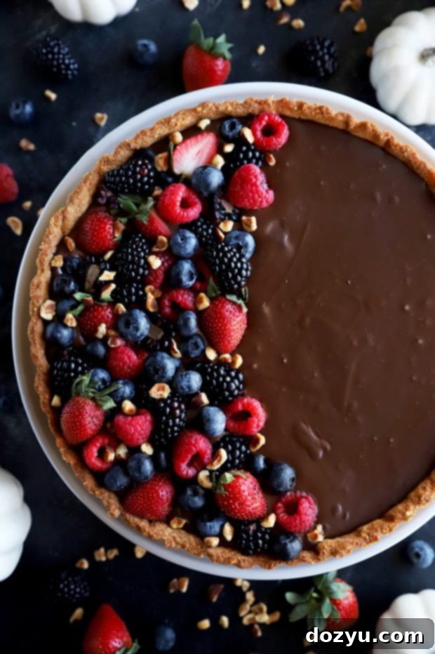 An overhead shot of the ganache tart, freshly topped with an abundance of colorful fresh berries and a sprinkle of chopped hazelnuts.