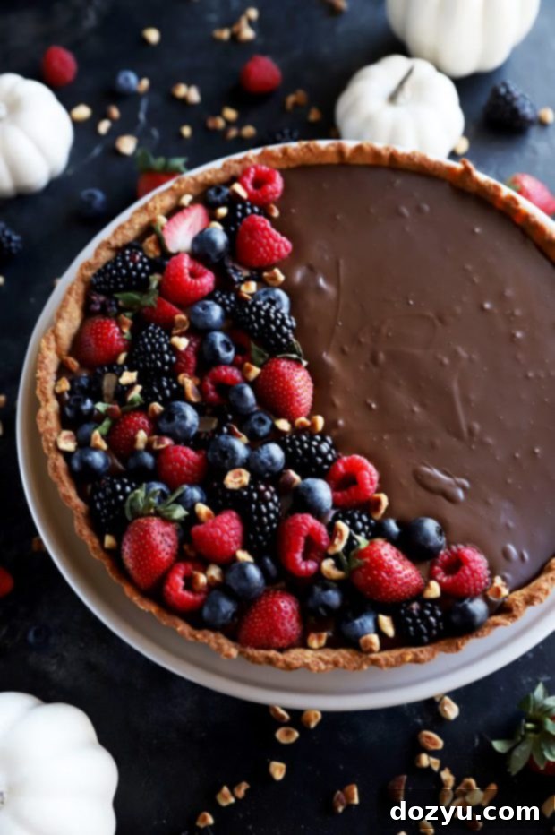 A chocolate tart with hazelnut crust, whole and perfectly set, displayed on a wooden surface.