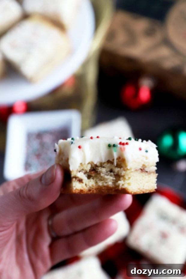 A hand holding a piece of chewy snickerdoodle cookie bar with eggnog frosting, showcasing a bite taken out