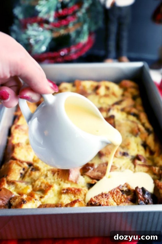 A hand gently pouring rich, creamy crème anglaise over warm slices of Panettone Bread Pudding in a baking dish, highlighting the indulgent topping.