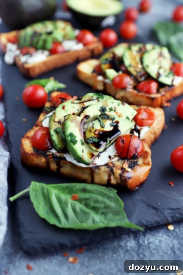 Close-up side view of a Caprese sandwich featuring melted mozzarella, fresh basil, and sliced tomatoes, with a hint of avocado in the background.