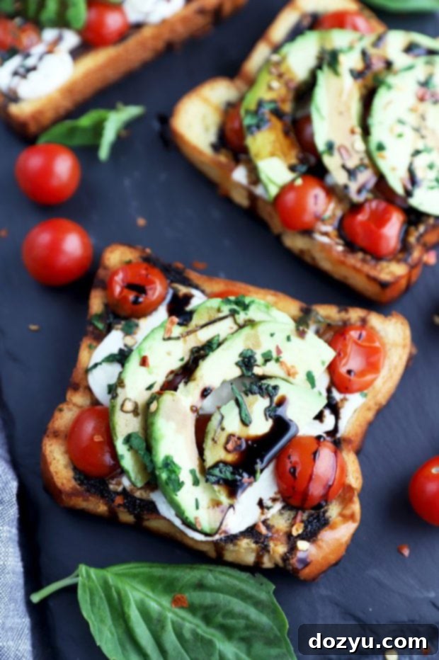 Top-down view of a grilled open-faced avocado Caprese sandwich, showcasing the fresh arrangement of basil, tomatoes, mozzarella, and avocado.