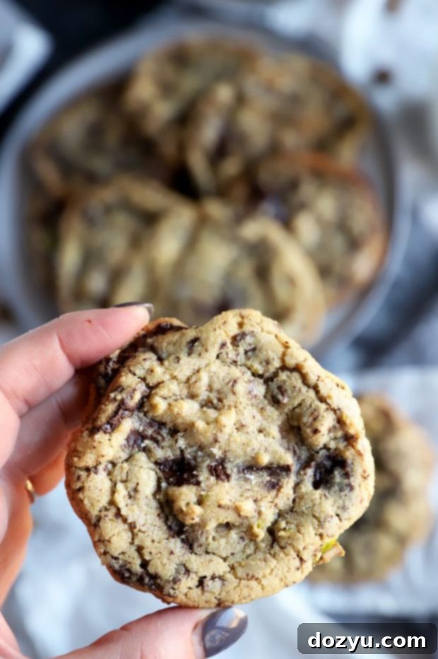 Hand holding a sea salt dark chocolate pistachio cookie, showing the rich chocolate and crunchy pistachios