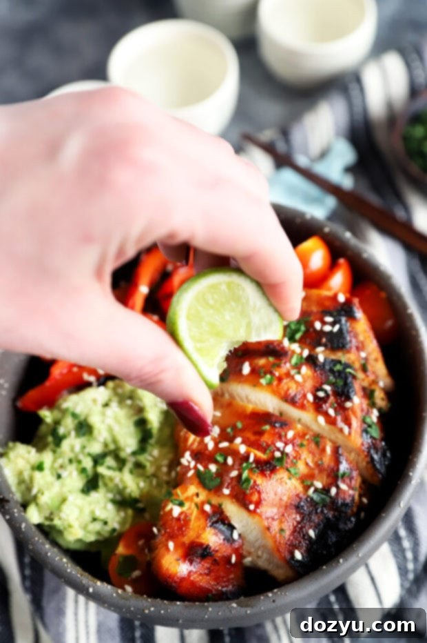 Hand squeezing lime over a vibrant Korean chicken rice bowl for extra freshness