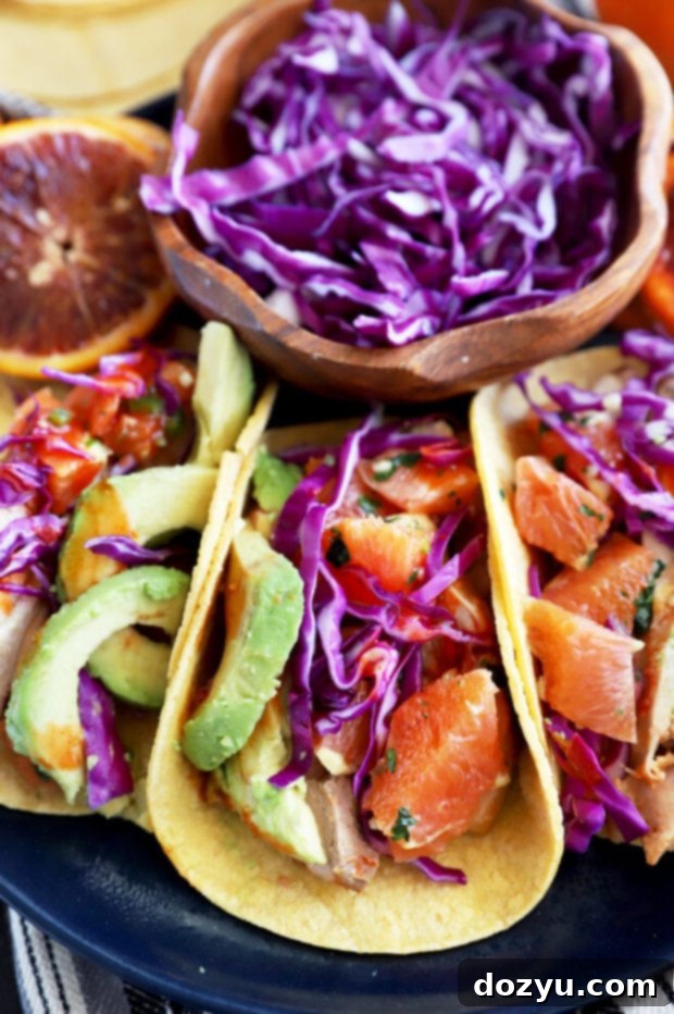 A vibrant close-up of two Blood Orange Honey Ginger Chicken Tacos resting on a dark plate, garnished with fresh cilantro and colorful salsa, highlighting the inviting textures and delicious ingredients.