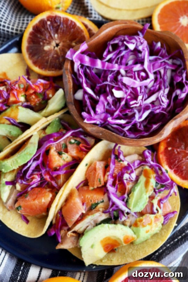 A top-down view of a plate filled with three Blood Orange Honey Ginger Chicken Tacos, garnished with fresh cilantro, hot sauce, and lime wedges, emphasizing their enticing presentation.