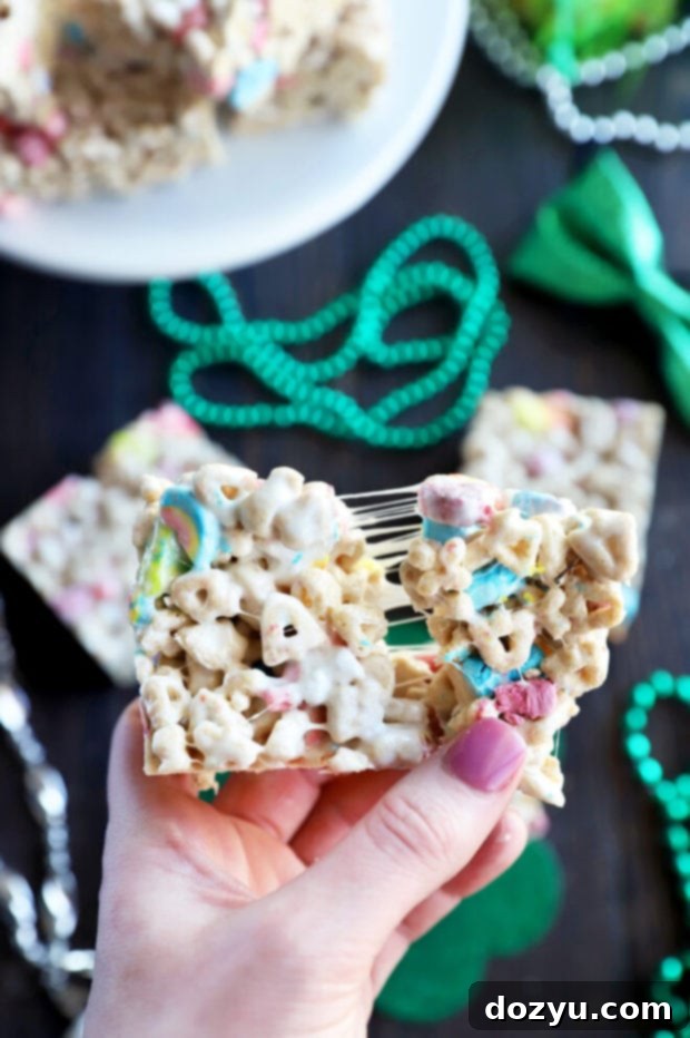 A hand pulling apart a sticky, gooey Lucky Charms cereal treat, showcasing its perfect marshmallow texture.