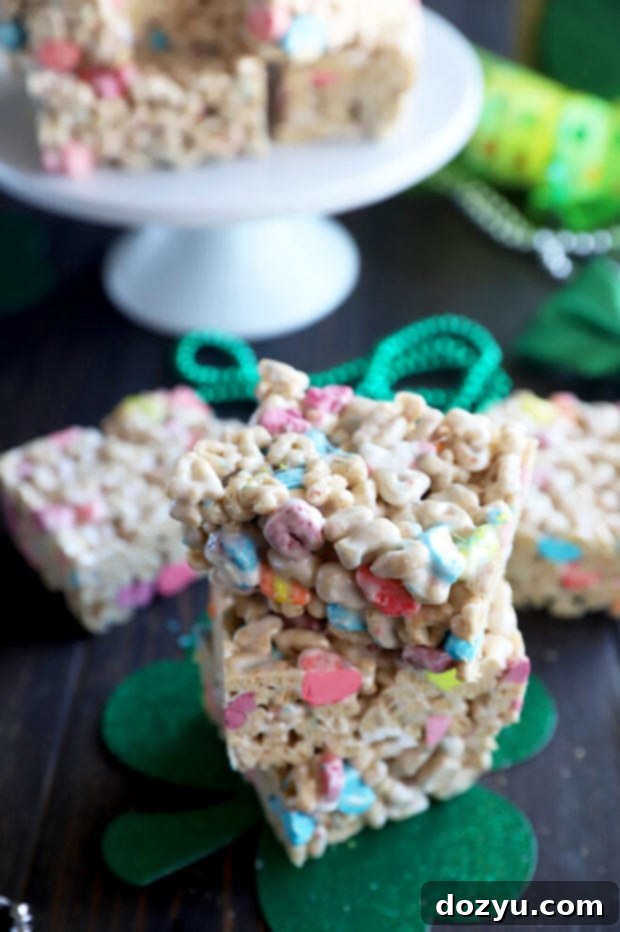 Stacked Lucky Charms cereal treats on a wooden board, garnished with extra colorful marshmallows.