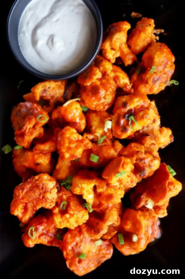 A plate piled high with crispy buffalo cauliflower, garnished and ready to eat