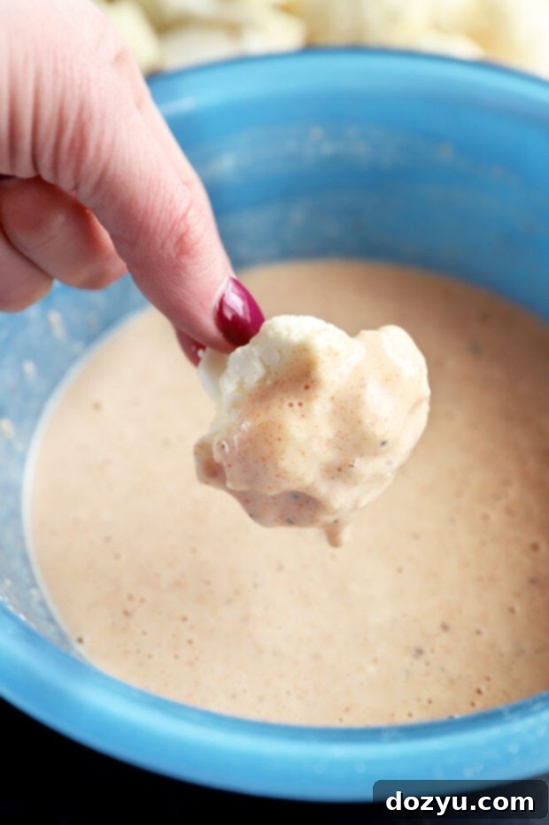 Cauliflower floret being dipped into a bowl of batter