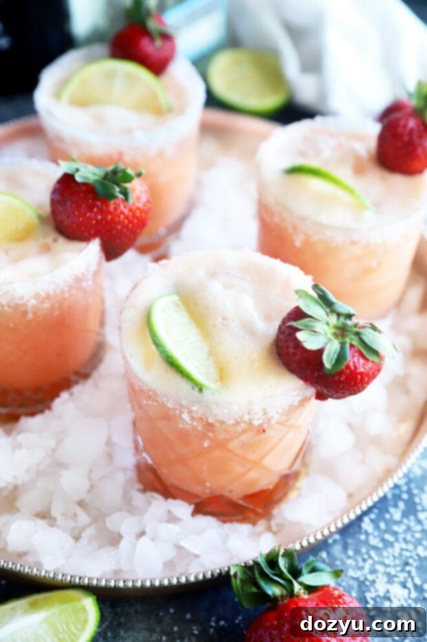 Two glasses of Strawberry Margarita Mimosas, garnished with fresh fruit, set against a light background, indicating readiness for serving