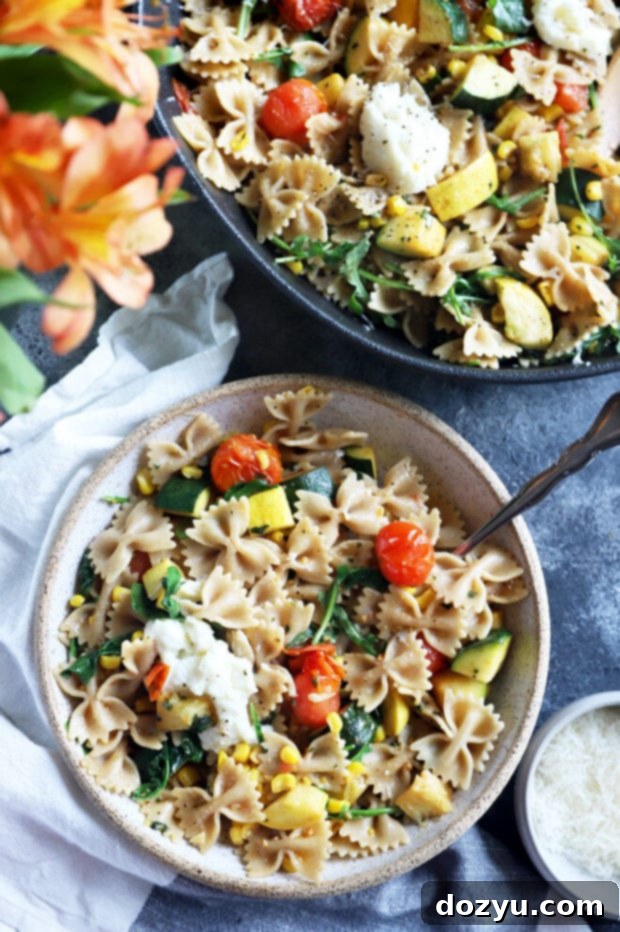 A beautifully styled photo of a summer dinner featuring farmer's market pasta in a bowl, with a fork, flowers, and linen.