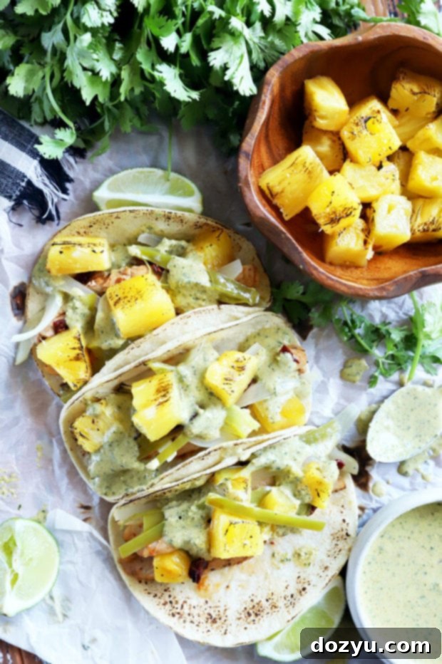 Overhead view of assembled pineapple chipotle chicken tacos with cilantro and lime wedges.