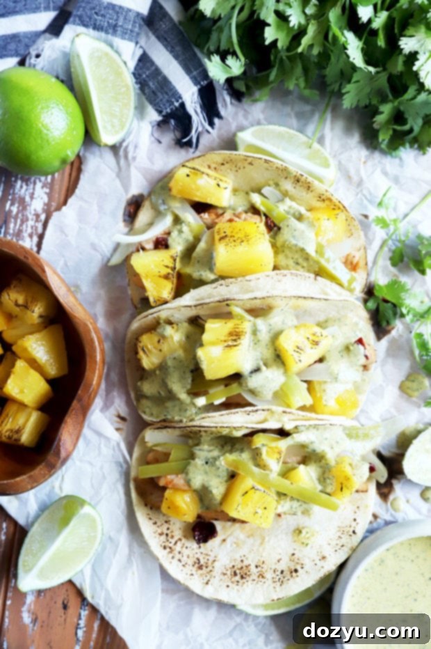 Overhead shot of assembled pineapple chipotle chicken tacos with sauce and fresh herbs.