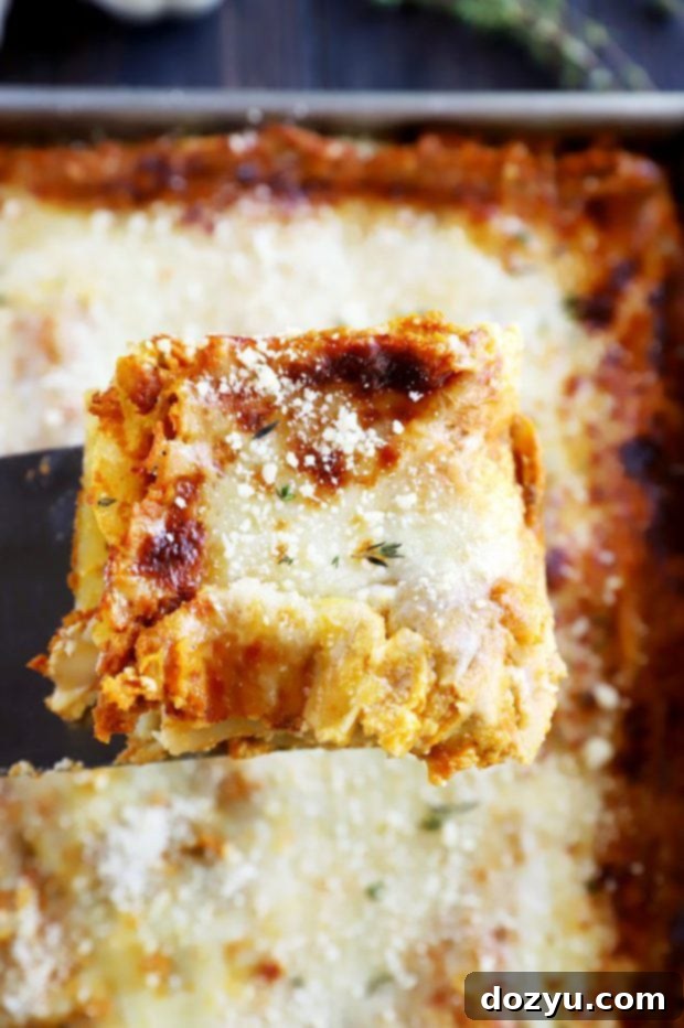 Lifting a golden brown piece of Freezer Spicy Herb Pumpkin Lasagna from the pan
