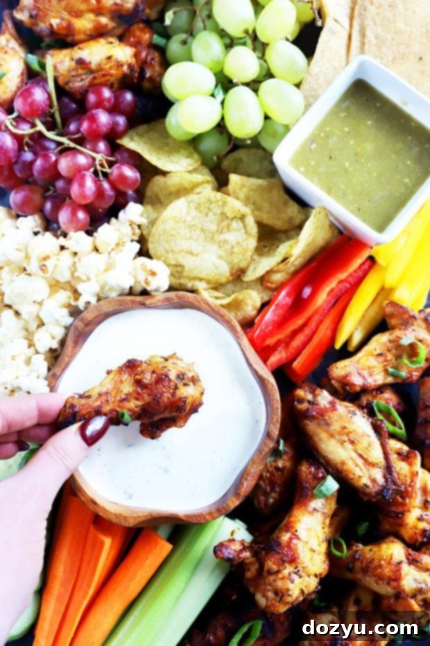 Hand dipping a grilled chicken wing into a creamy cilantro sauce over a snack board